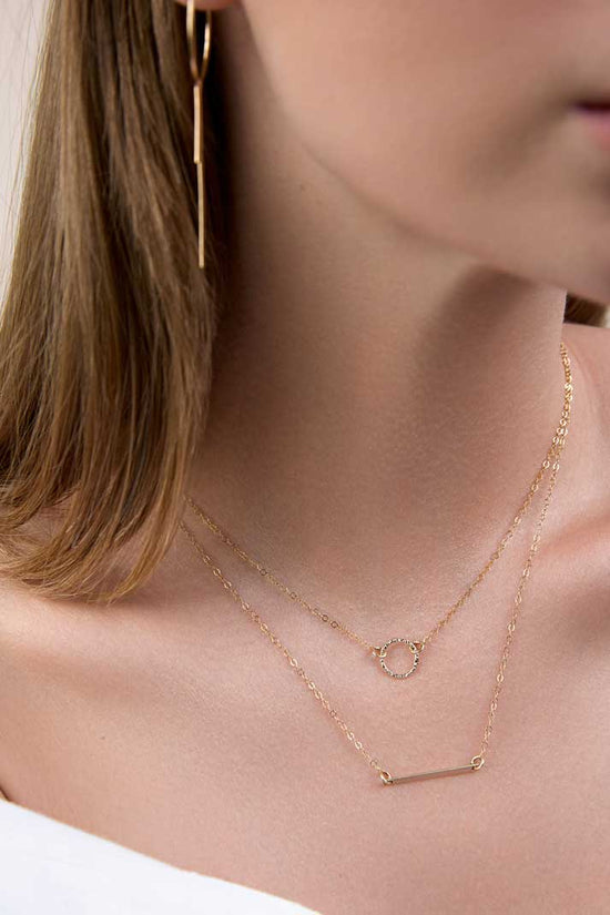 Girl wearing dainty gold circle and bar stackable necklaces