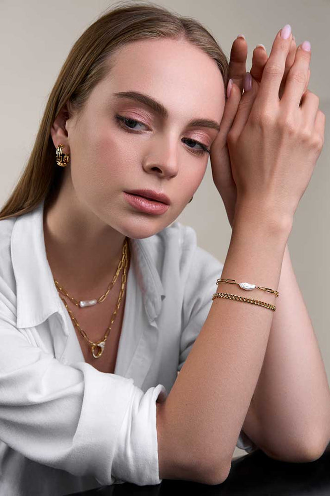 
                  
                    Girl with white button down shirt wearing gold layered bracelets and necklaces
                  
                