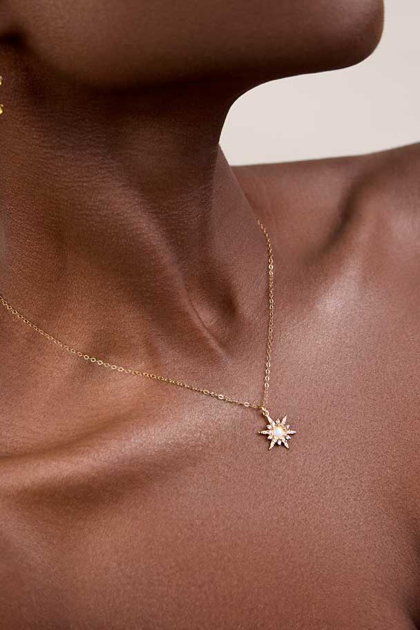 Neck showing a sunburst gold charm with white opal in the center